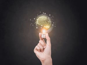 A hand holding a light bulb with a brain drawing